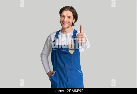 Painting Works. Young Handyman With Paintbrush In Pocket Showing Thumb Up Stock Photo