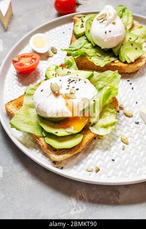 Healthy sandwich - poached eggs and avocado on toast with tomatoes on concrete background. Stock Photo