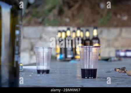 Two almost empty cups of wine. Blurred beer bottles in the background. Remains of rubbish and trash of public drinking in parks. Concept of youth and Stock Photo