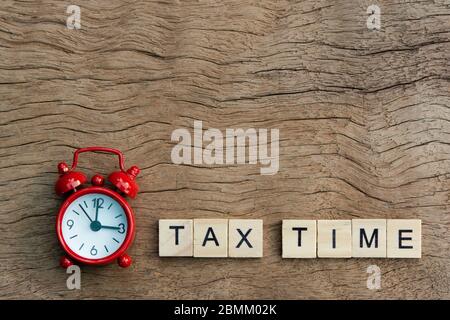 Red alarm clock and Tax time with wooden alphabet blocks, on plank wooden background with copy space Stock Photo