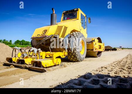 Vibration plate compactor is mounted to the steamroller, compacting sand at road construction site. Stock Photo