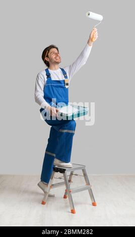 Painting Services Concept. Worker Holding Paint Roller, Applying Dye To Ceiling Stock Photo