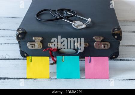 retro style suitcase with compass and medical stethoscope. Colorful sticky notes with space for an inscription. The concept of safe holidays and famil Stock Photo