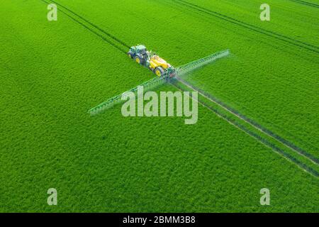 Green Fields. Aerial view of the tractor spraying the chemicals on the large green field. Agricultural spring background. Stock Photo