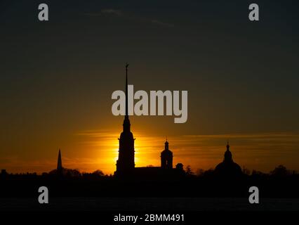 The  silhouette of Peter and Paul Fortress in St. Petersburg, Russia in the rays of setting sun on the yellow, orange and red background of sky Stock Photo
