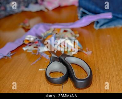 29 Crafting at home. Close up and selective focus of a pair of crafting scissors and fabric, in soft focus, on a wooden table during a sewing project Stock Photo