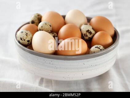 Selection of chicken and quail eggs in a bowl on a table with a white cloth. Stock Photo