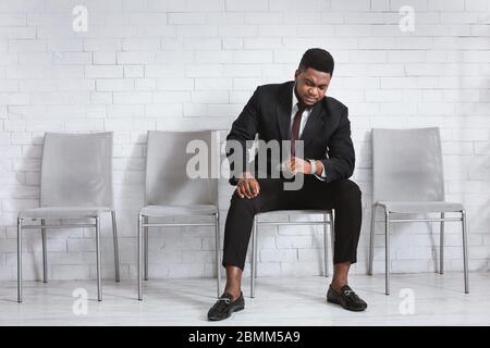 Millennial African American guy waiting for job interview, looking at his watch in office lobby. Empty space Stock Photo