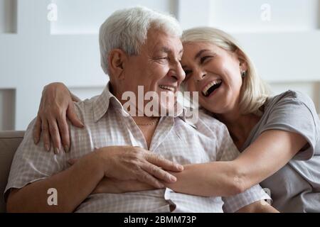 Happy senior couple relax on couch hugging Stock Photo