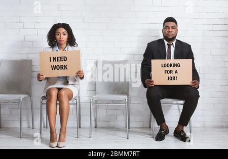 African American guy and girl with cardboard signs waiting for job interview in company hall Stock Photo