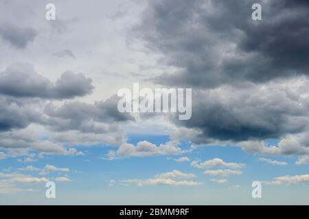 Dark thunderclouds are approaching the blue sky with white clouds. Change of weather from sunny to rainy. Dramatic skyscape. Low angle view. Stock Photo