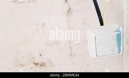 one white light switch in paint and putty is temporarily hanging on a black wire during repair against the background of an unfinished wall. open the Stock Photo