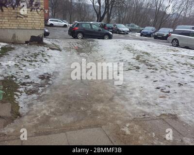 Pedestrian path covered in snow, water and mud. Parking lot in the background Stock Photo