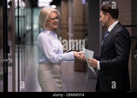Businesspeople meet in office hallway shake hands greeting each other Stock Photo