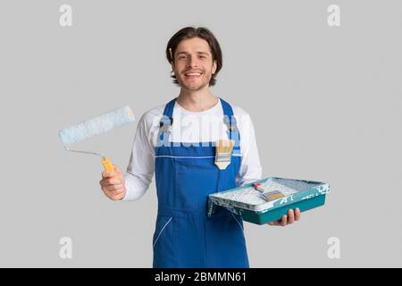 Renovation Services. Smiling Painter In Uniform With Painting Tools In Hands Stock Photo