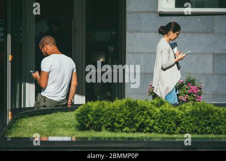 Moscow, Russia - AUGUST 31, 2017: A young man and woman stand and use their phones keeping a social distance from each other on the streets of a Stock Photo