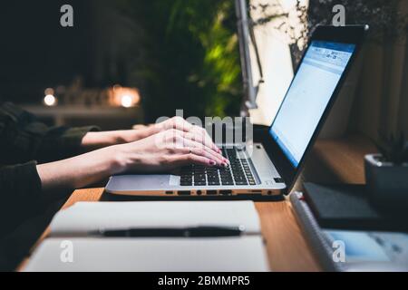 Hands of a woman using laptop computer working overtime at his desk in the office late at night. Work from home concept with notebook and pen Stock Photo