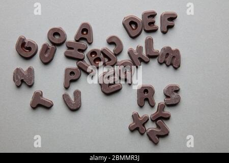 an artsy studio shot of mixed chocolate letters against a grey background Stock Photo