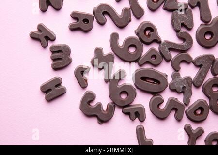 an artsy studio shot of chocolate letters and numbers against a pastel pink  background Stock Photo
