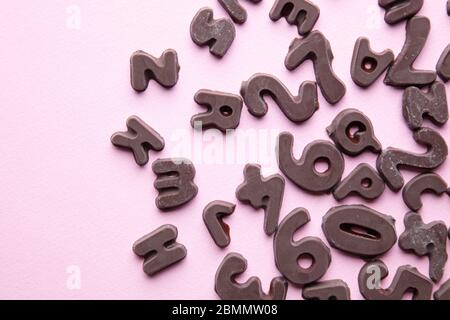 an artsy studio shot of chocolate letters and numbers against a pastel pink  background Stock Photo
