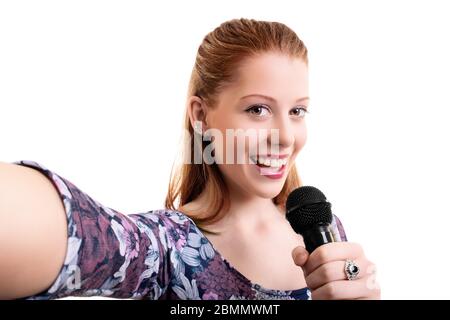 Beautiful young girl holding a microphone and taking a selfie, isolated on white background. Lifestyle, happiness, and social concept. Stock Photo