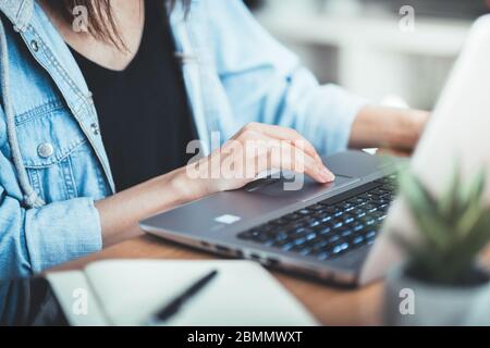 Cropped image of woman working at her office via laptop, young female manager using portable computer device while sitting at desk, flare light, work. Stock Photo