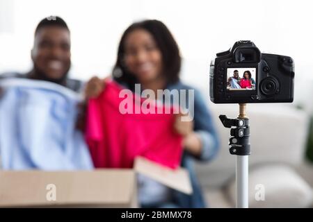 Camera Recording Video Of Fashion Bloggers Couple Unboxing Parcel With New Clothes Stock Photo