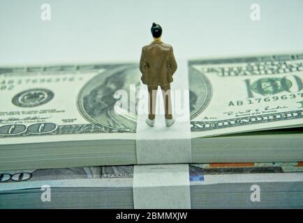 Figure of a man in a suit on top of a wad of hundred dollar bills in a white background Stock Photo