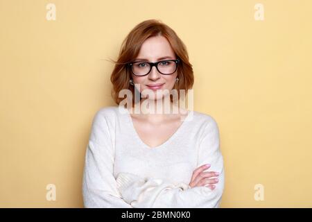 Close up of studio portrait of cheerful satisfied successful woman with short hair wears glasses, white oversize sweater, poses, smiling, arms crossed Stock Photo