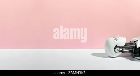 Closeup of abstract white robot lying down on white surface against pink background Stock Photo