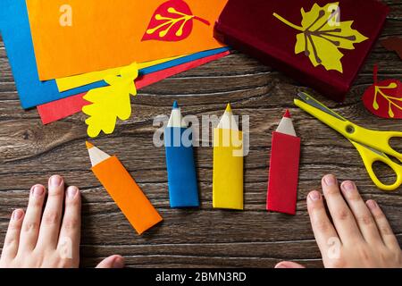 Child holds multi-colored bookmarks origami pencil made of paper new school year on a wooden table. Welcome to school. Children's art project, needlew Stock Photo