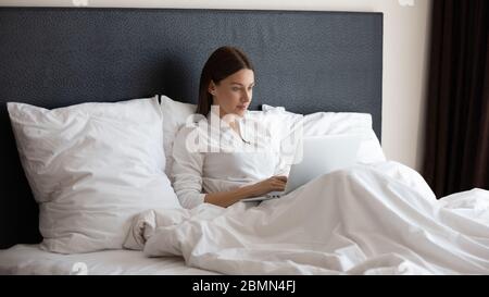 Woman sitting on bed using computer check email in morning Stock Photo