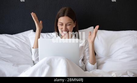 In morning woman sitting in bed with laptop feels happy Stock Photo