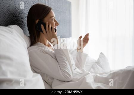 Rested awakened woman sitting in bed talking on phone Stock Photo