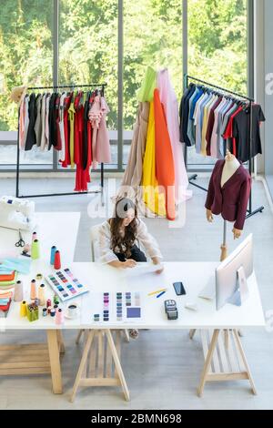 Top view of young adult asian fashion designer drawing and sketching her work at home as atelier studio with colour palette. Using for entrepreneur sm Stock Photo