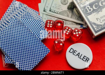 Poker cards, red dices and stack of dollars with white dealer sign on red background Stock Photo