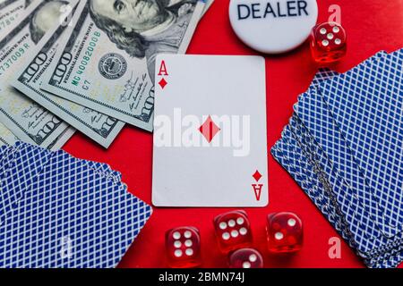 Poker cards, red dices and stack of dollars with white dealer sign on red background Stock Photo