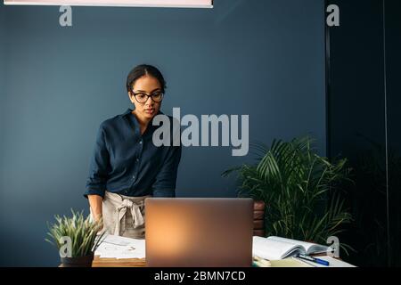 Serious businesswoman looking on a laptop screen while standing at a table Stock Photo