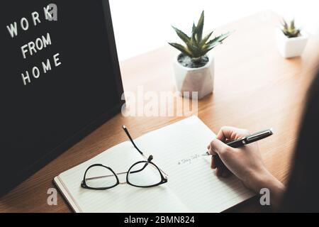 Back view of woman hand with pencil writing stay safe on notebook at home desk. Work from home and quarantine concept on epidemic outbreak. Stock Photo