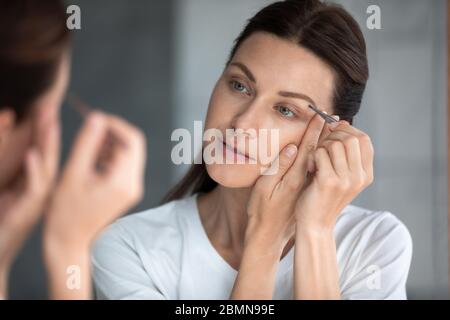Closeup portrait gorgeous woman holding tweezers plucks eyebrows Stock Photo