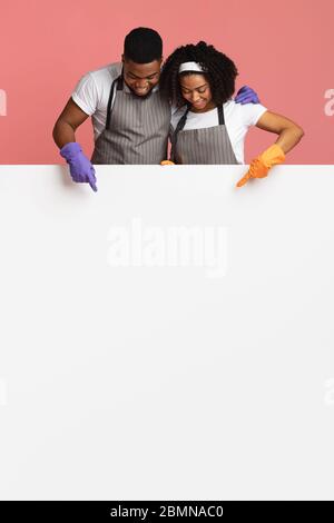 Cleaning Service Offer. Happy African Couple Pointing At White Advertisement Board Stock Photo