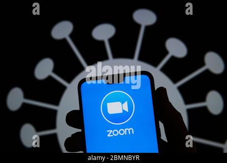 Stone / United Kingdom - May 10 2020: Zoom app logo on a smartphone silhouette hold in hand. Coronavirus image on the blurred background. Real photo, Stock Photo