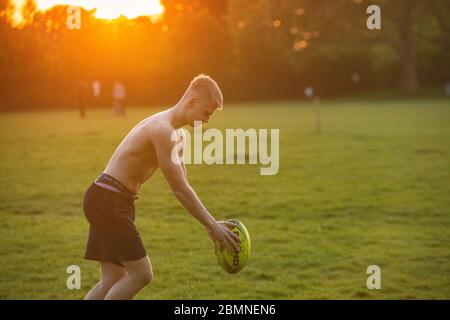 A muscly teenager plays rugby at sundown in a London park Stock Photo