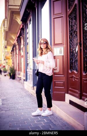 Full lenght shot of smiling mature woman text messaging while walking on the street in the city. Stock Photo