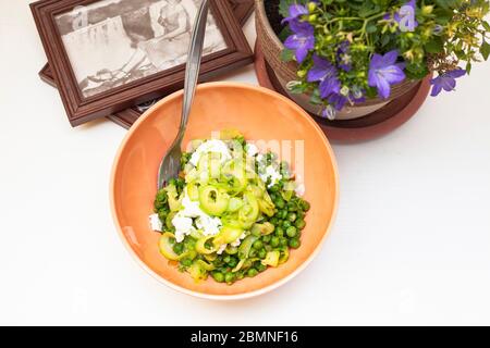 Zucchini spaghetti with peas and ricotta in natural light with a beautiful plant with purple flowers and two small squares nearby Stock Photo