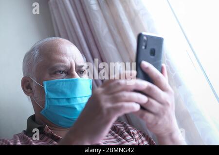 senior man with face mask using smart phone indoor  Stock Photo