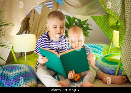 Two cute brothers reading books in a children's tent. 6 years old boy and baby toddler Stock Photo