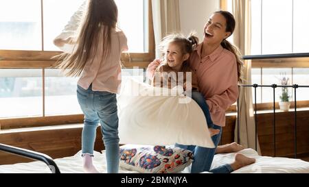 Happy little girls with mother pillow fighting in bedroom Stock Photo