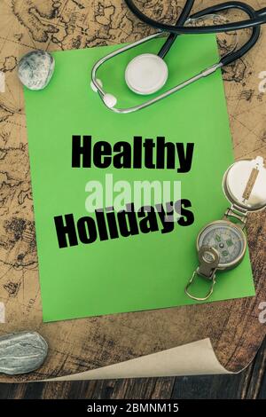 stethoscope, compass and a card with the words 'Healthy Holidays' on the background of an old map of the world, The concept of safe travel Stock Photo