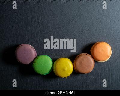 Five macaroons of different colours arranged in the form of a smile on a black slate plate Stock Photo